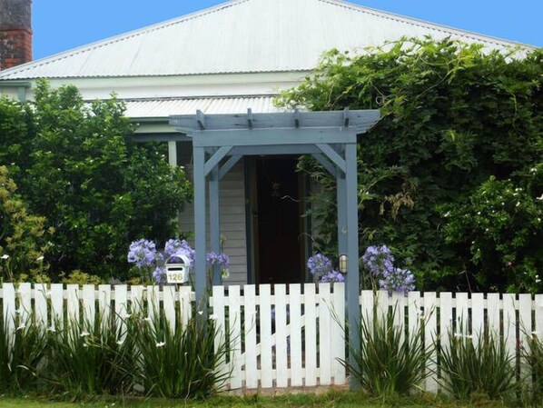 A house with a white picket fence, a covered porch, and purple flowers in the front yard.