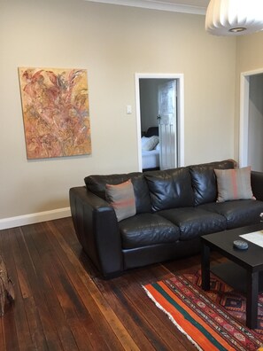 A living room with a black leather sofa, a patterned rug, and a large abstract painting on the wall.