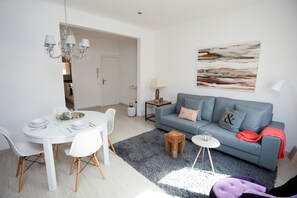 Una sala moderna con un sofá gris, una mesa de comedor blanca y una araña.