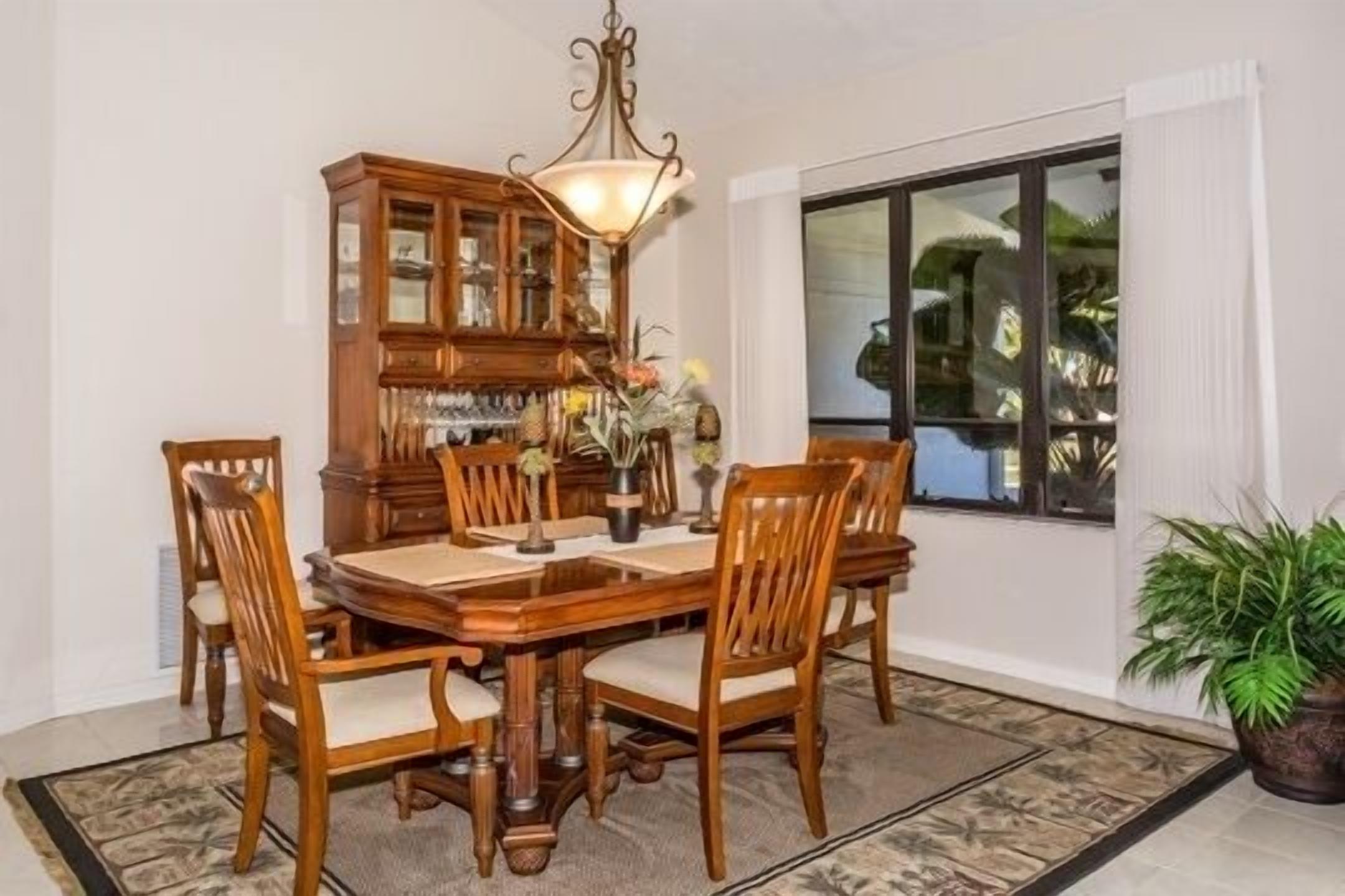 A dining room with a wooden table and chairs, a cabinet with glass doors, and a hanging light fixture.
