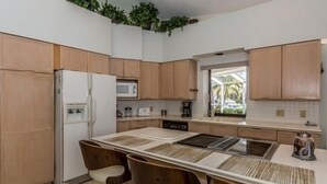 Eine moderne Küche mit Holzausstattung, einer zentralen Kochinsel inklusive Barhocker, einem Kühlschrank, einer Mikrowelle und einer Kaffeemaschine.