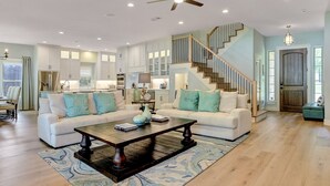 A spacious living room with a large sofa set, a coffee table, and a staircase leading to an upper level.