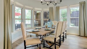 A dining room with a large table, six upholstered chairs, and a chandelier.