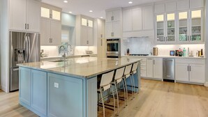 A modern kitchen with white cabinetry, a central island with bar stools, stainless steel appliances, and a dishwasher.