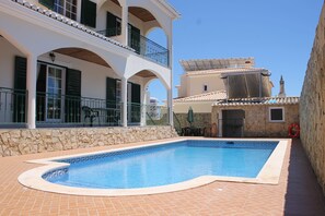 A swimming pool with a tiled deck, a stone wall, and a building with balconies and a solar panel. - HOME SOUSA tranquility for your holiday in family 10 minutes from the beach !! (Lagos)