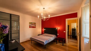 Ein Schlafzimmer mit einem Bett, einem Schreibtisch, einem Stuhl, einer Chandelier und einer roten Wand.