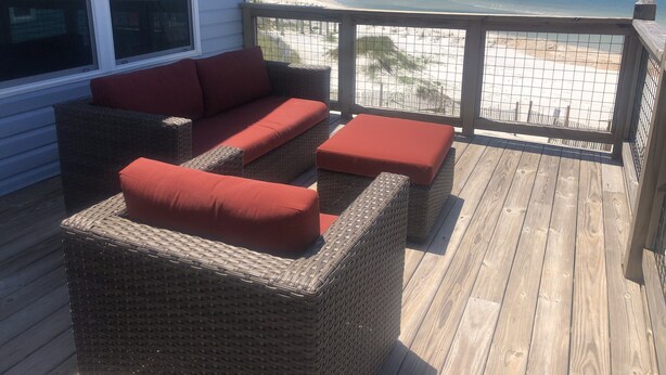 Une terrasse en bois, meublée de meubles en osier, avec vue sur la plage.