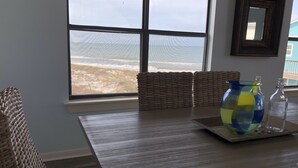 Un coin repas avec une grande fenêtre, des chaises en osier, une table en bois et un vase en verre décoratif.