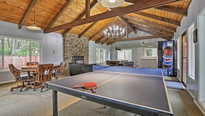 A ping pong table in a room with a stone wall, wooden ceiling beams, and a chandelier. - Lincoln City Condo: Pool Access, Walk to Beach! (Lincoln City)