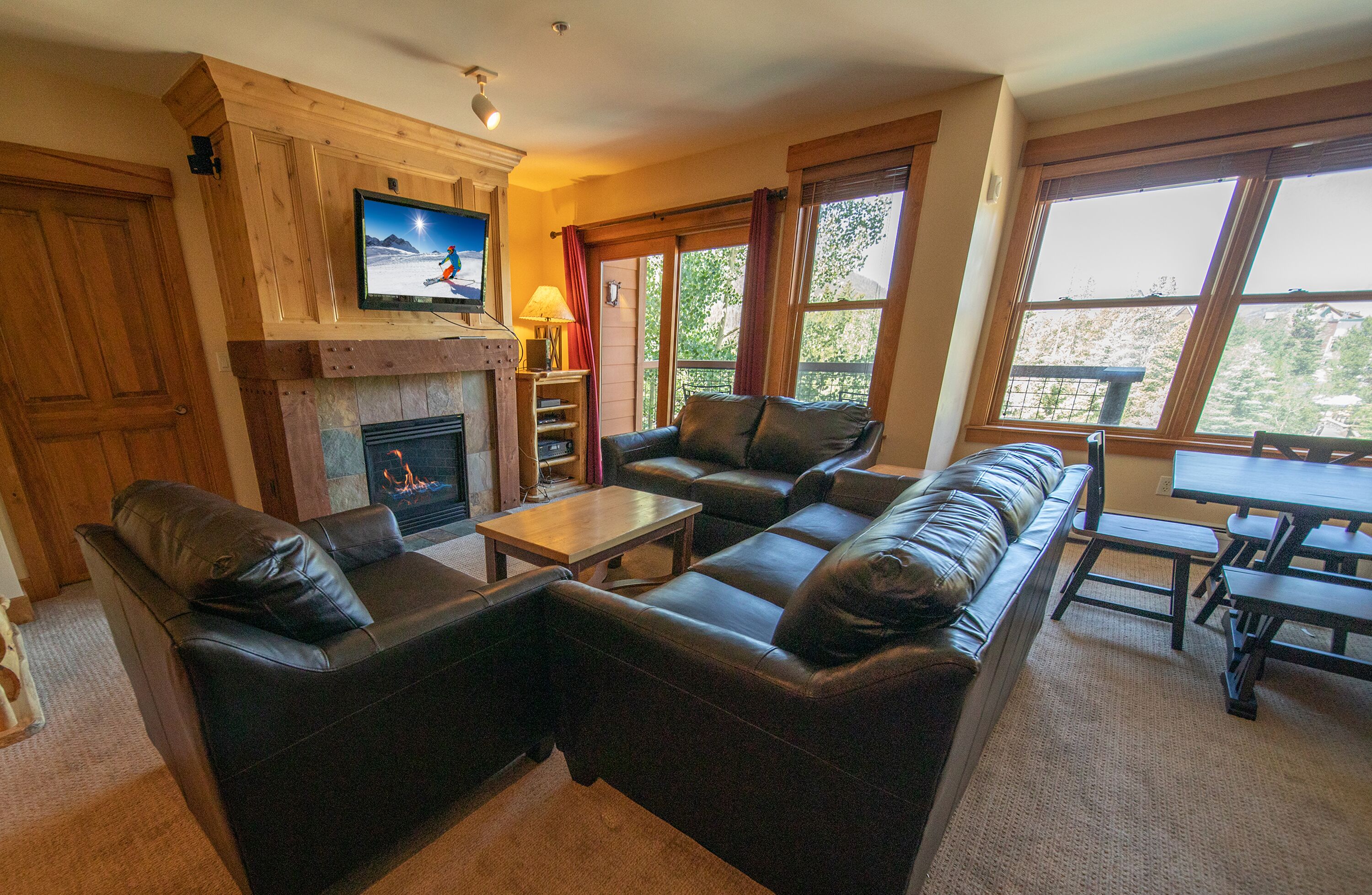 A cozy living room with a fireplace, leather sofas, a TV mounted on a wooden cabinet, and a dining area with a table and chairs.