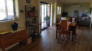 A cozy living room with a wooden dining table, chairs, a TV, and a sofa. - Hunter Valley Rural Lodge - Quaint towns, State forests & Wineries to explore! (Glendon Brook)