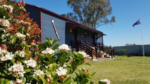 A building with a corrugated metal exterior, a wooden staircase, and a flagpole with the Australian flag. - Hunter Valley Rural Lodge - Quaint towns, State forests & Wineries to explore! (Glendon Brook)