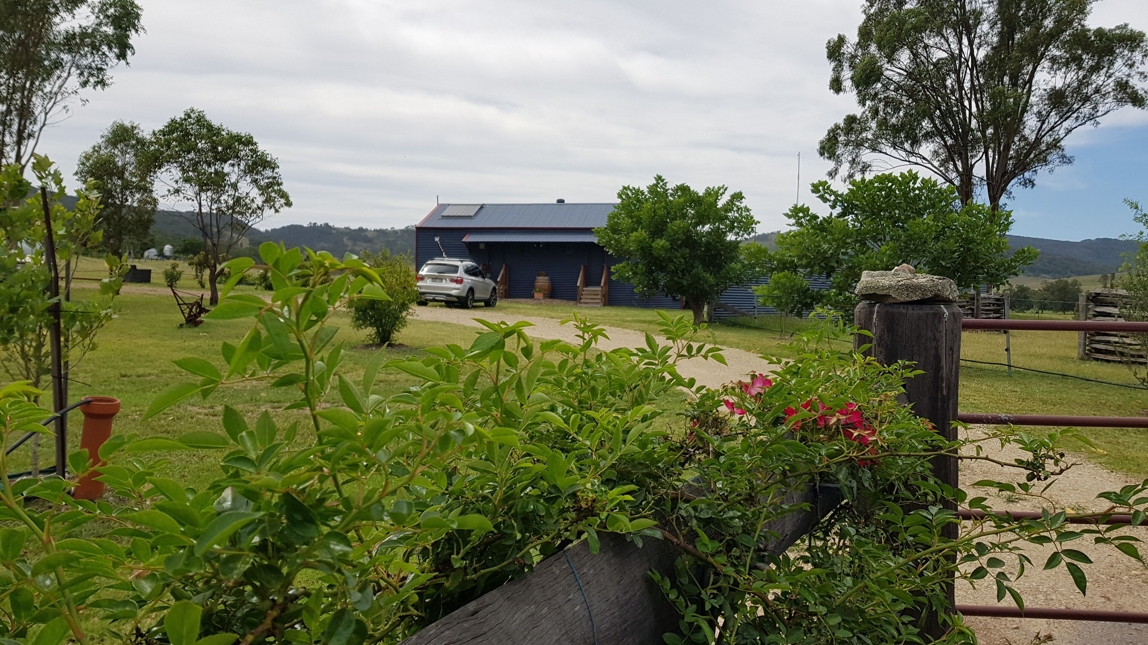 Uma propriedade rural com um grande celeiro, um carro estacionado na frente e uma área cercada com vegetação.