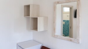 Une salle de bain avec des toilettes blanches, un miroir avec un cadre en bois et une étagère fixée au mur.