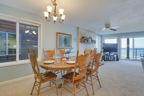 A dining area with a round table, wooden chairs, and a chandelier. There is a television and a ceiling fan in the background. - Cozy Oregon Resort Condo - Steps to Lincoln Beach! (Lincoln City)