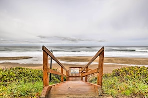 Eine Holztreppe führt zu einem Strand, oben ist ein Schild zu sehen.