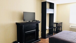 A hotel room with a fireplace, a television, a bed, and a small table. - Langham Motel (Langham)