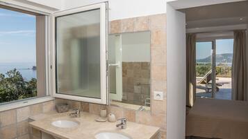Une salle de bain avec deux lavabos, un grand miroir et une vue sur la mer.