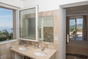 A bathroom with two sinks, a large mirror, and a view of the sea.