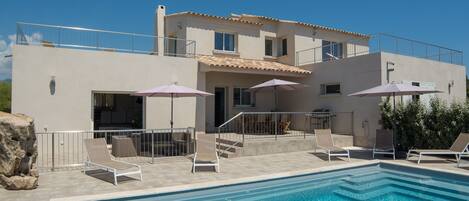 A modern two-story house with a swimming pool, outdoor seating, and a covered patio area.