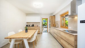 A modern kitchen with white cabinets, a wooden dining table, and a view through an open door. - Ca l'Apostol, Mallorca style villa with a swimming pool (Pollença)