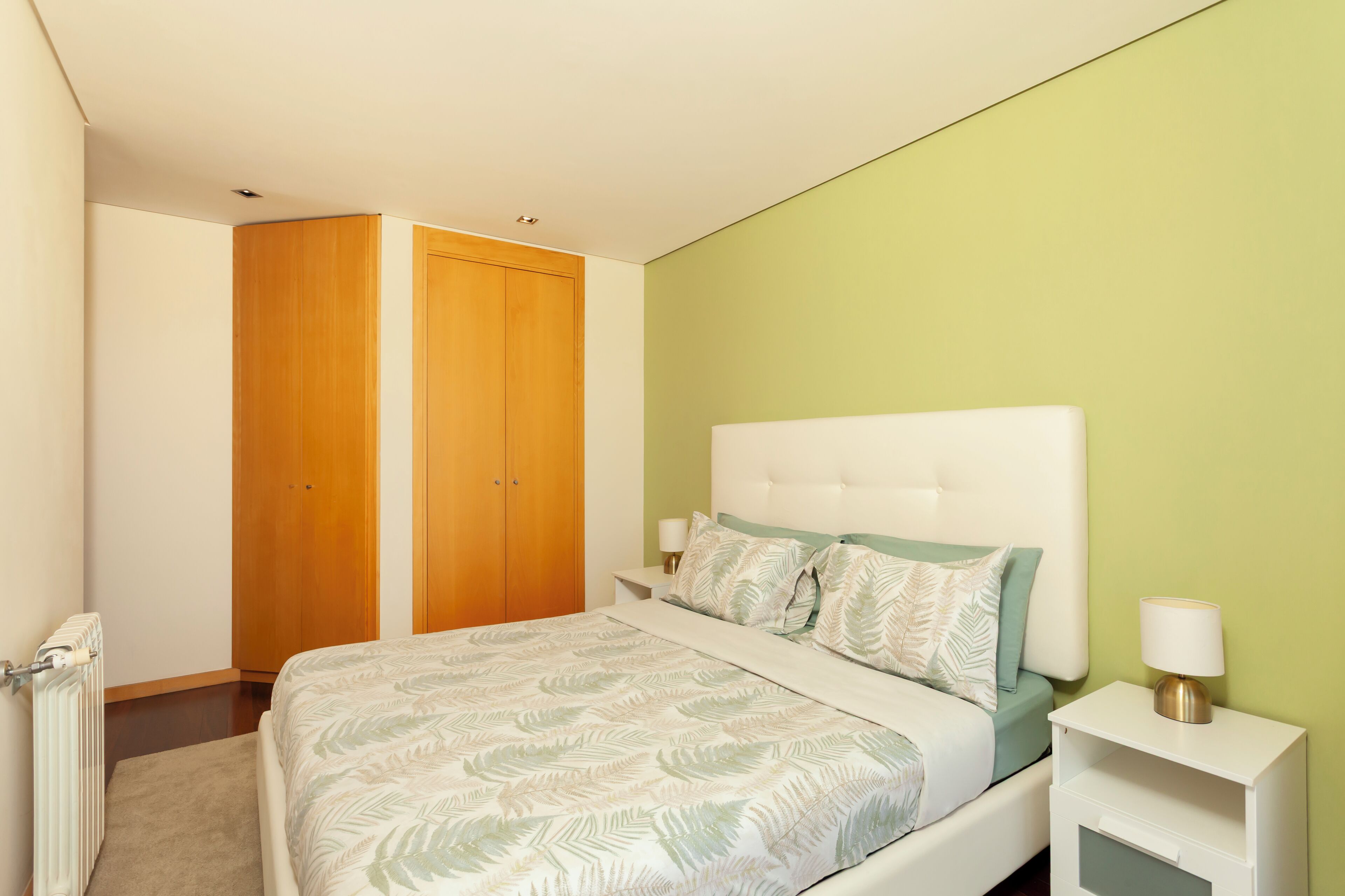 Een slaapkamer met een bed, nachtkastjes, een houten kledingkast en een groene wand.
