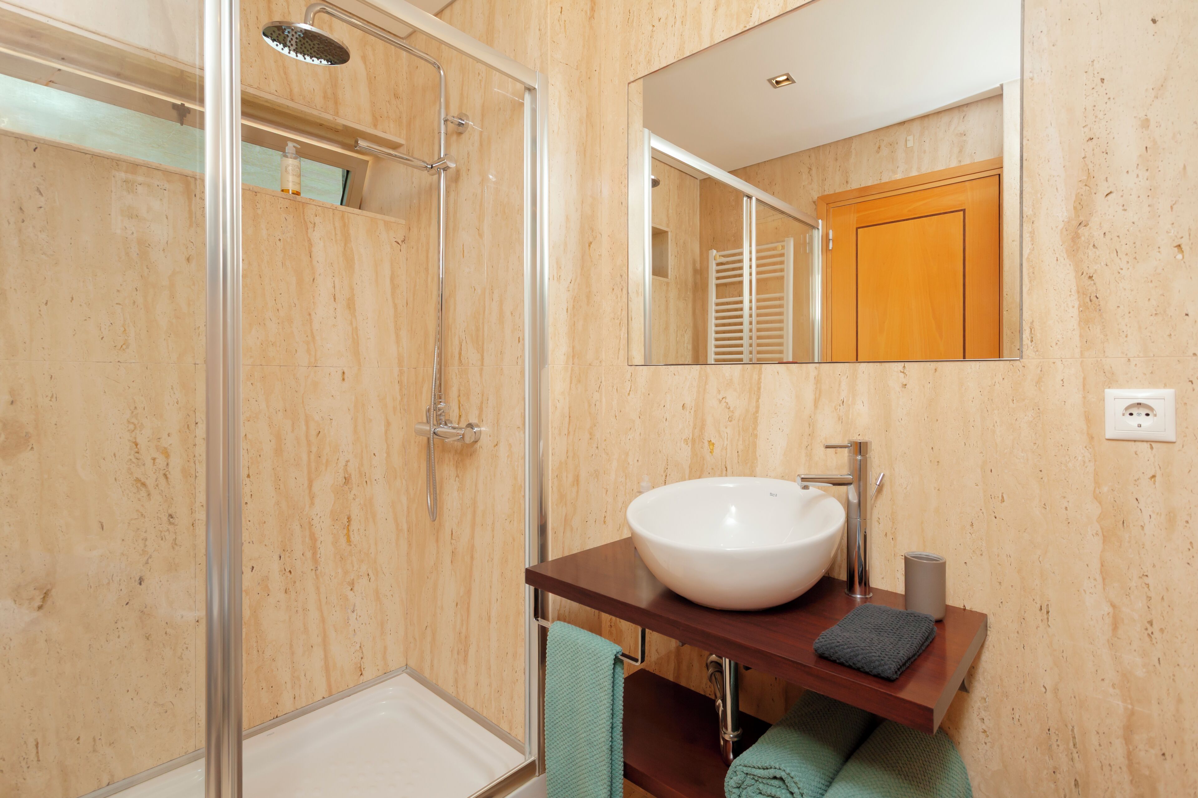 A modern bathroom with a glass-enclosed shower, a white sink, and a wooden vanity.