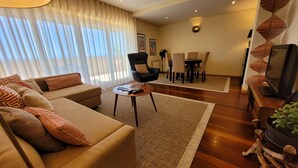 A living room with a sofa, armchairs, a coffee table, a dining area with chairs, a television, and a plant. - Beach and City Getaway (Vila Nova de Gaia)