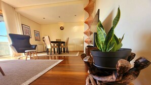 A modern living room with a dining area, wooden flooring, a potted plant, and a unique wooden stand. - Beach and City Getaway (Vila Nova de Gaia)