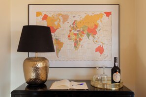 Un mapa mundial enmarcado, una lámpara, un libro abierto y una botella sobre una mesa.