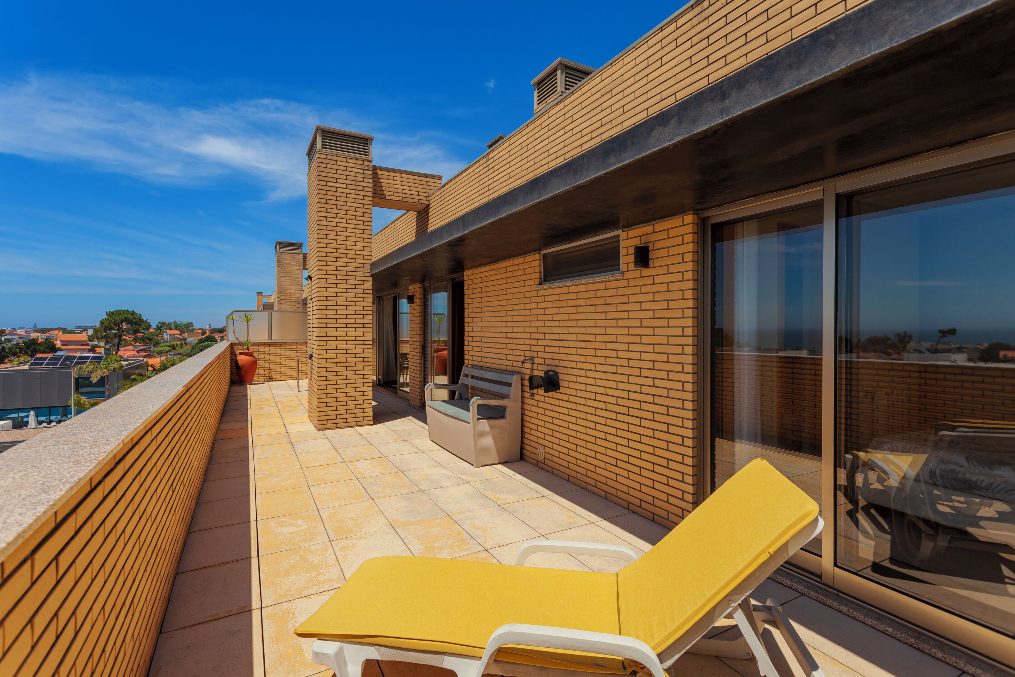 Una terrazza sul tetto con una poltrona gialla, un barbecue e una porta vetrata che dà su un balcone.