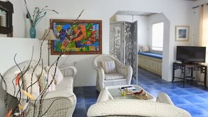 A living room with two wicker sofas, a coffee table, a painting, and a TV on a stand. - Crew's Nest at Bayview Villas, Poolside Studio close to Grafton Beach (Black Rock, Pleasant Prospect)