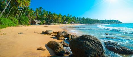 Enjoy the serene beach scene with ocean waves gently crashing onto the shore, surrounded by palm trees and thatched-roof huts.