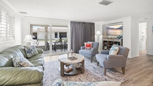 A living room with a green sofa, a grey armchair, a round coffee table, and a TV on the wall. - Island House Beach Resort V5 (Siesta Key)