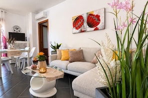 A modern living room with a sofa, a glass coffee table, and a painting on the wall.