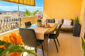 A balcony with a table, chairs, a sofa, and potted plants.