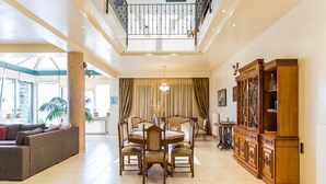 Un salón amplio con techo alto, un comedor con mesa redonda y un gran aparador de madera.