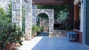 Un arco de piedra que da acceso a un patio con plantas en macetas y una mesa.