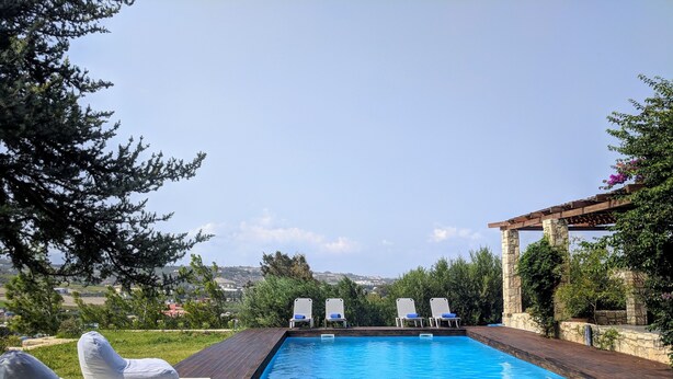 Una piscina rectangular con terraza de madera y sillas de descanso blancas.