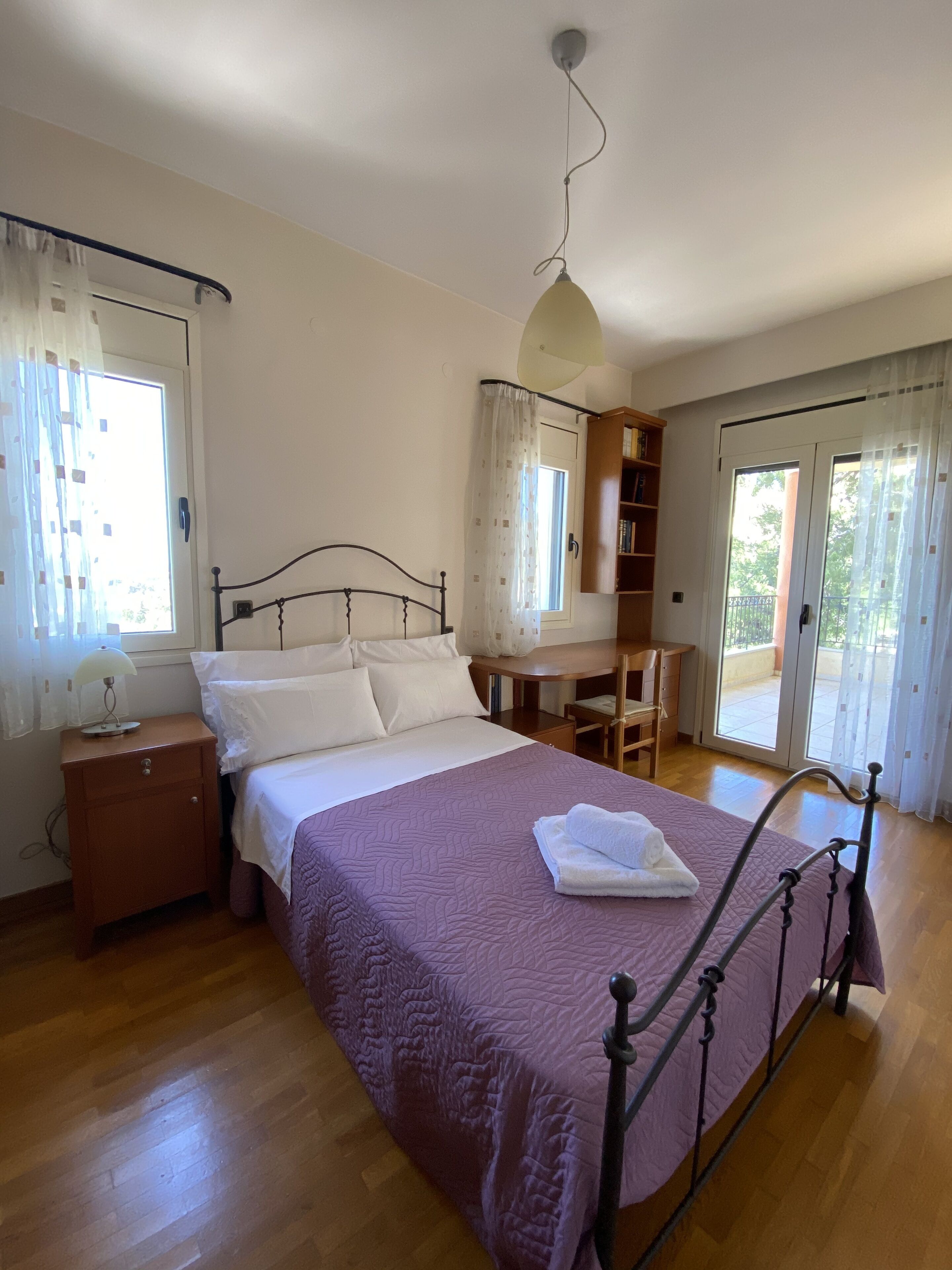 A bedroom with a bed, bedside table, lamp, and a desk with chair.