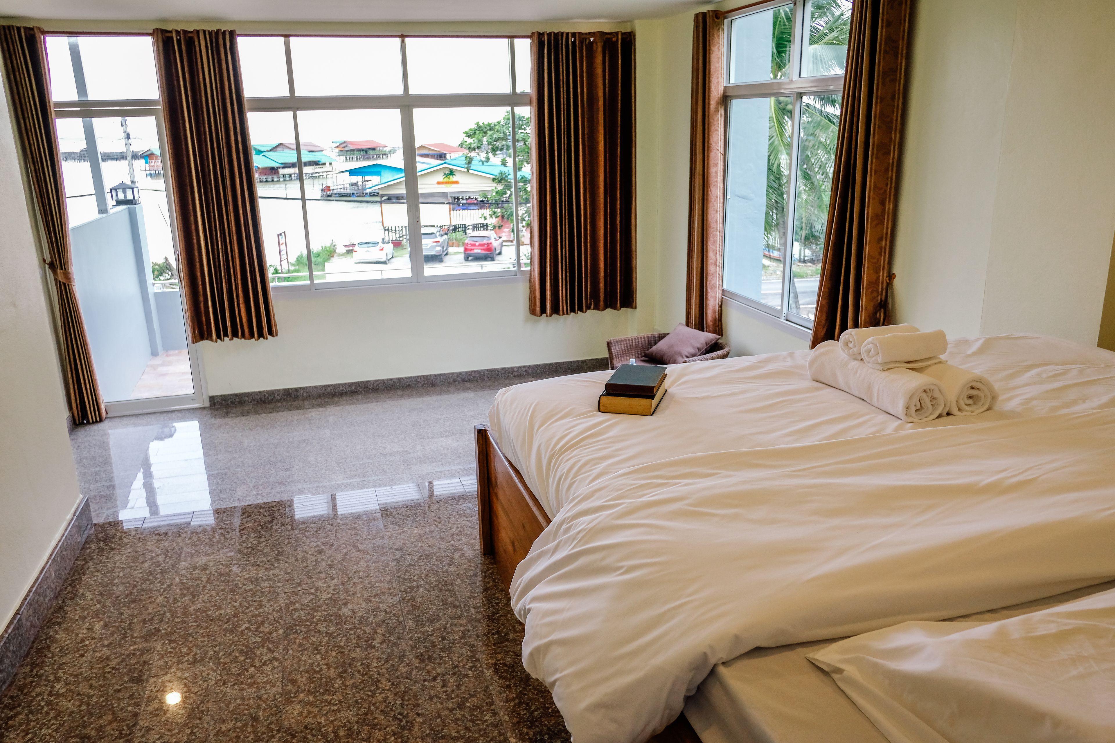 A hotel room with a large bed, a chair, a window with curtains, and a view of the outside.