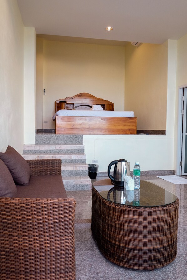 Une chambre d’hôtel avec un lit, un canapé en osier, une table basse en verre et une bouteille d’eau.