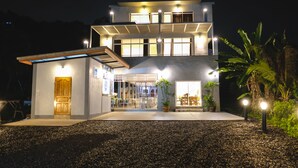 Une maison moderne à deux étages, dotée d’un patio couvert, d’une porte en bois et d’une entrée bien éclairée.