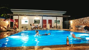 Une piscine intérieure où des personnes nagent et se détendent, entourée d’un patio couvert avec des tables et des chaises.