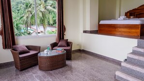 A room with a wicker sofa, a small round table, a bed with a wooden headboard, and a view of palm trees through a window. - The Lake House Ko Yo (Songkhla)