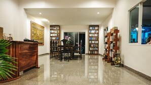 A spacious, well-lit hallway with a polished granite floor, flanked by wooden bookshelves filled with books and decorative items. A wooden desk with a vase of flowers is positioned on the left, and a staircase is visible in the background. - The Lake House Ko Yo (Songkhla)