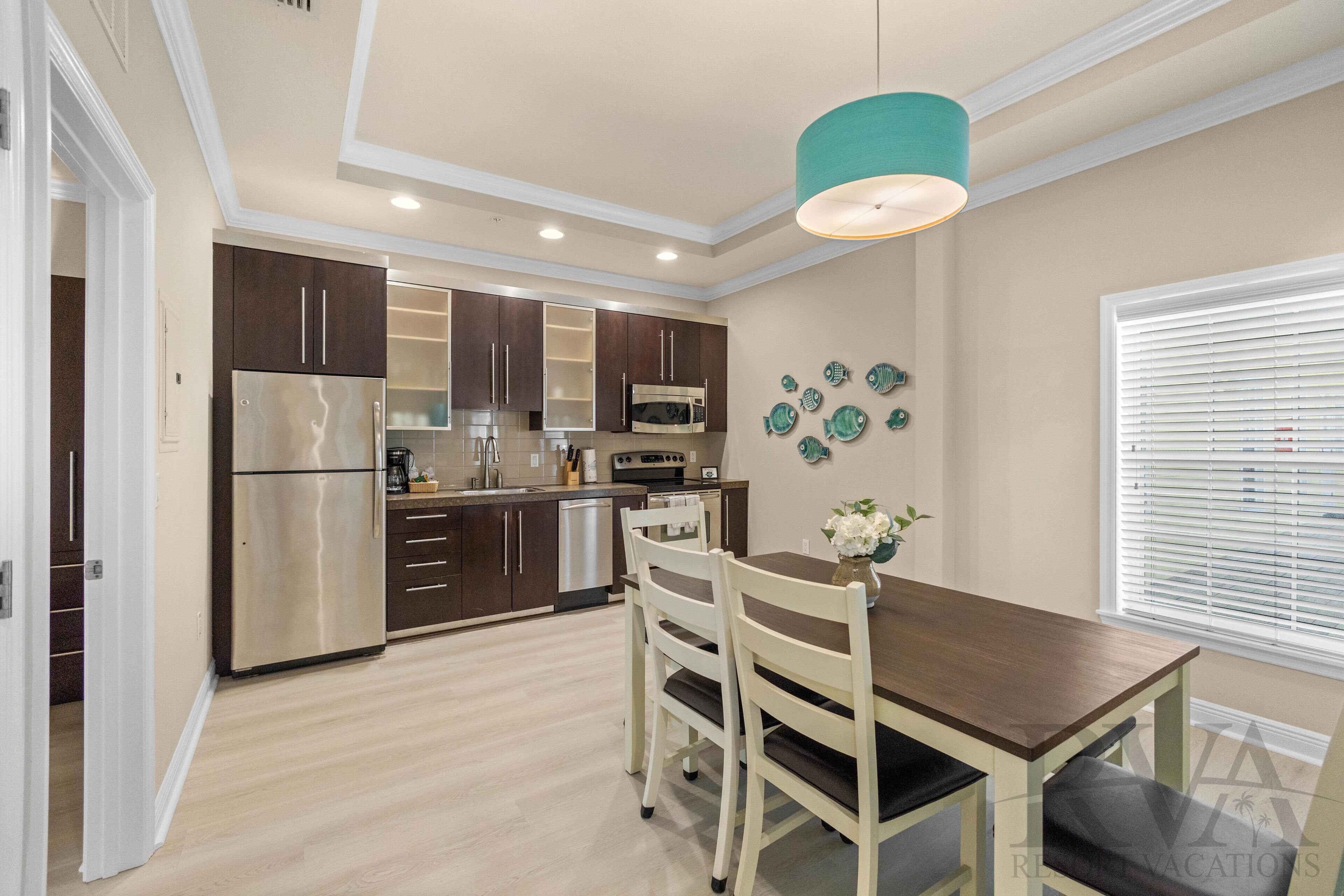 A modern kitchen with dark cabinets, stainless steel appliances, and a dining area with a wooden table and chairs.