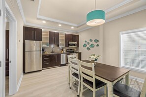 A modern kitchen with dark cabinets, stainless steel appliances, and a dining area with a wooden table and chairs.