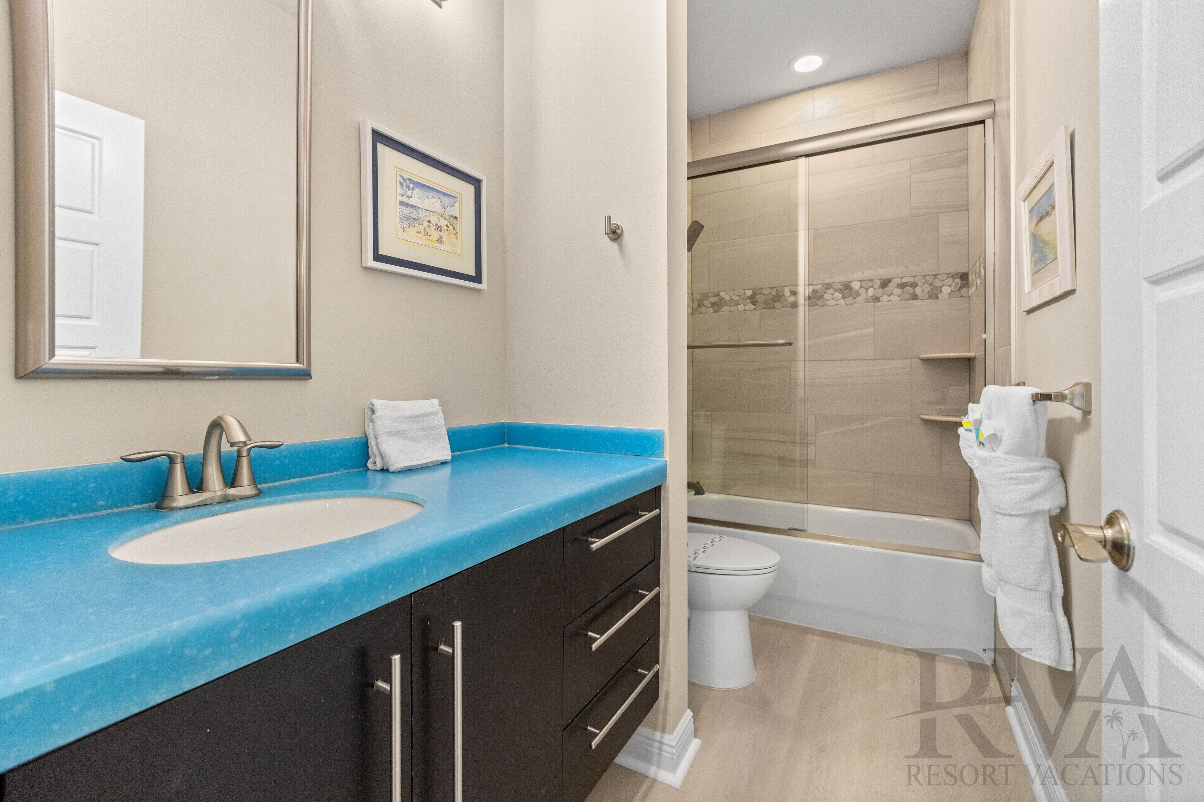 Une salle de bain avec un lavabo bleu, des toilettes blanches et une douche à parois de verre.