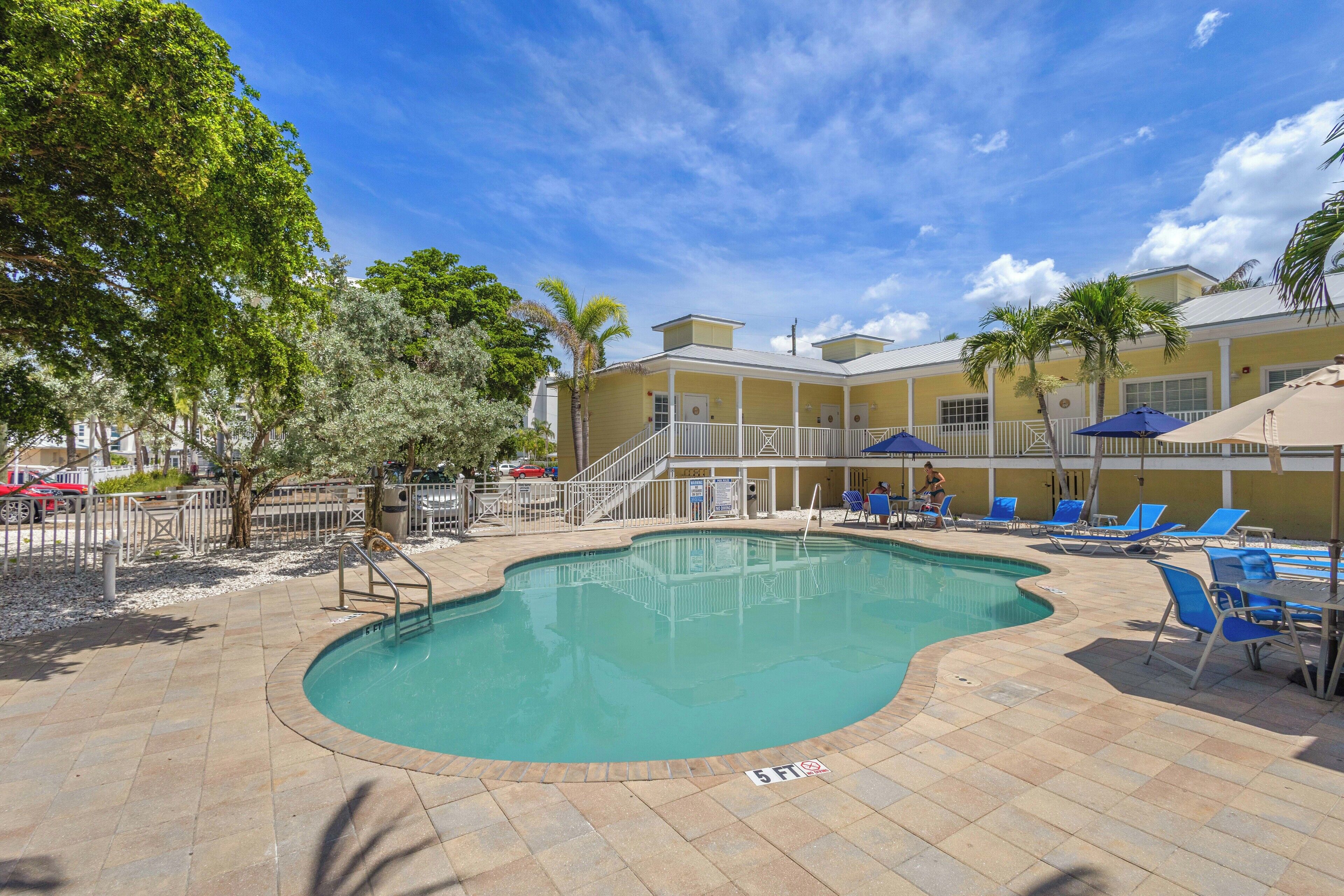 A swimming pool with a 5ft depth marker, surrounded by lounge chairs and palm trees.